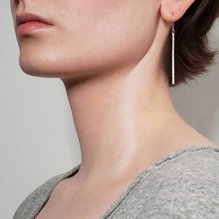 Left facing woman wearing long silver bar earrings with hammered texture hung on sterling ear wires