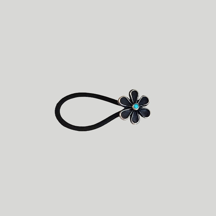 Sterling silver flower with turquoise center attached to a large black hair rubber band. 