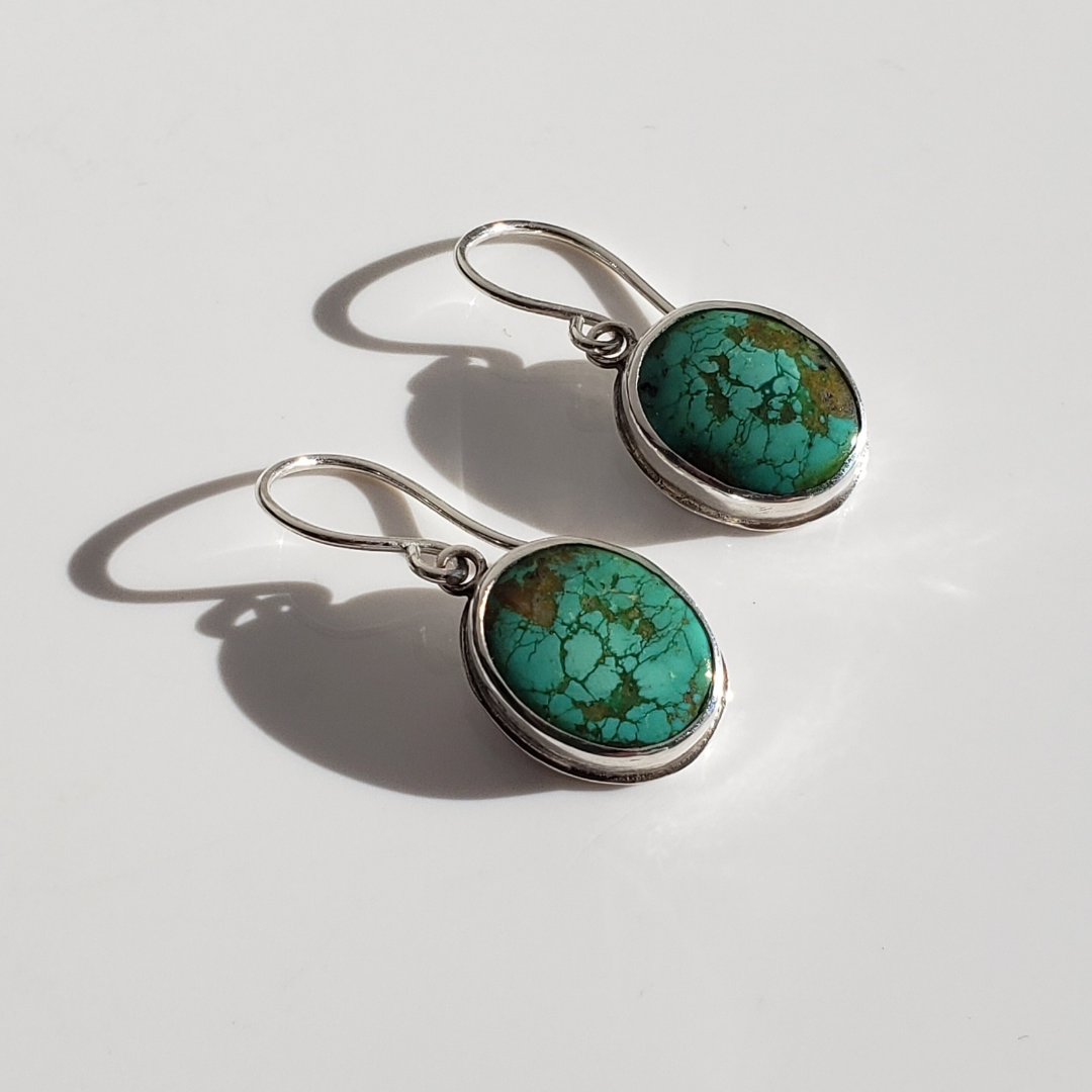 Green turquoise and sterling silver drop earrings against white background