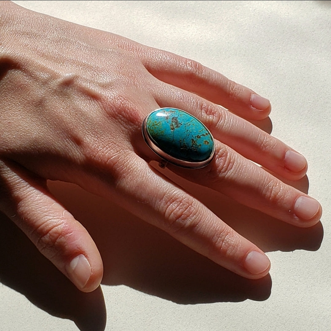 Right facing woman hand wearing large oval turquoise gemstone ring on middle finger 