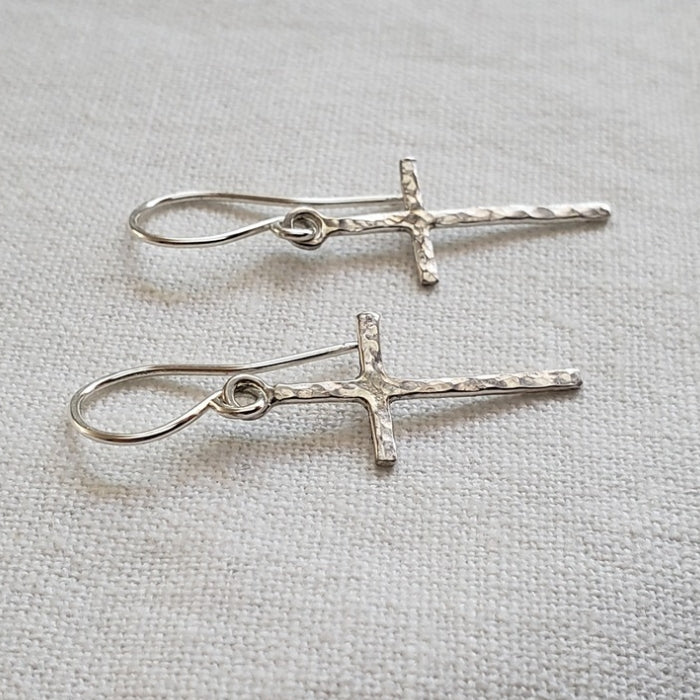 Small silver cross earrings with hammered texture hung from artisan wires 