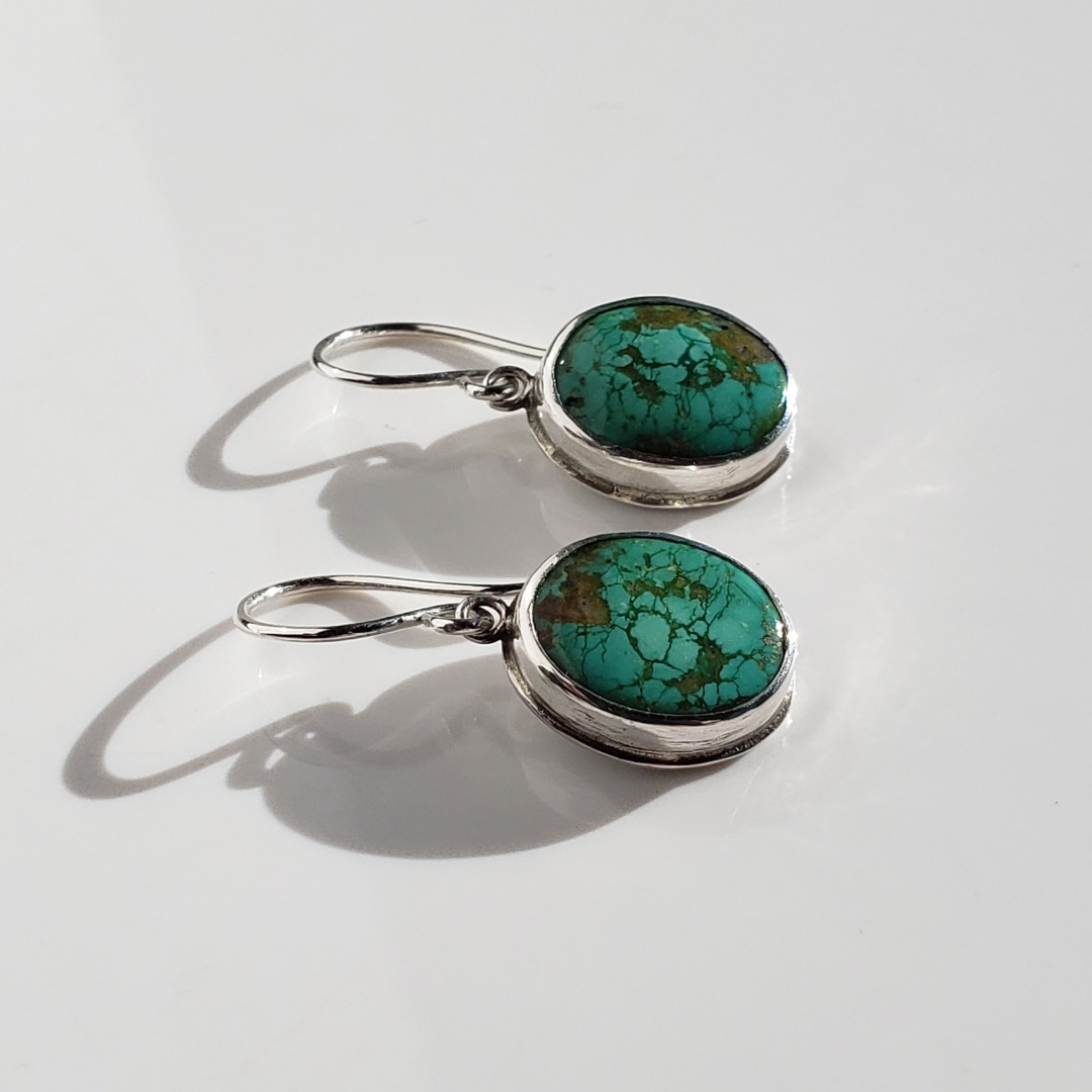 Green turquoise and sterling silver drop earrings against white background