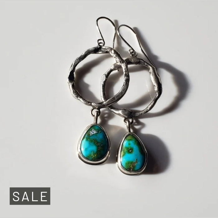 a pair of large turquoise and sterling silver hoop earrings laying on a gray background for display.