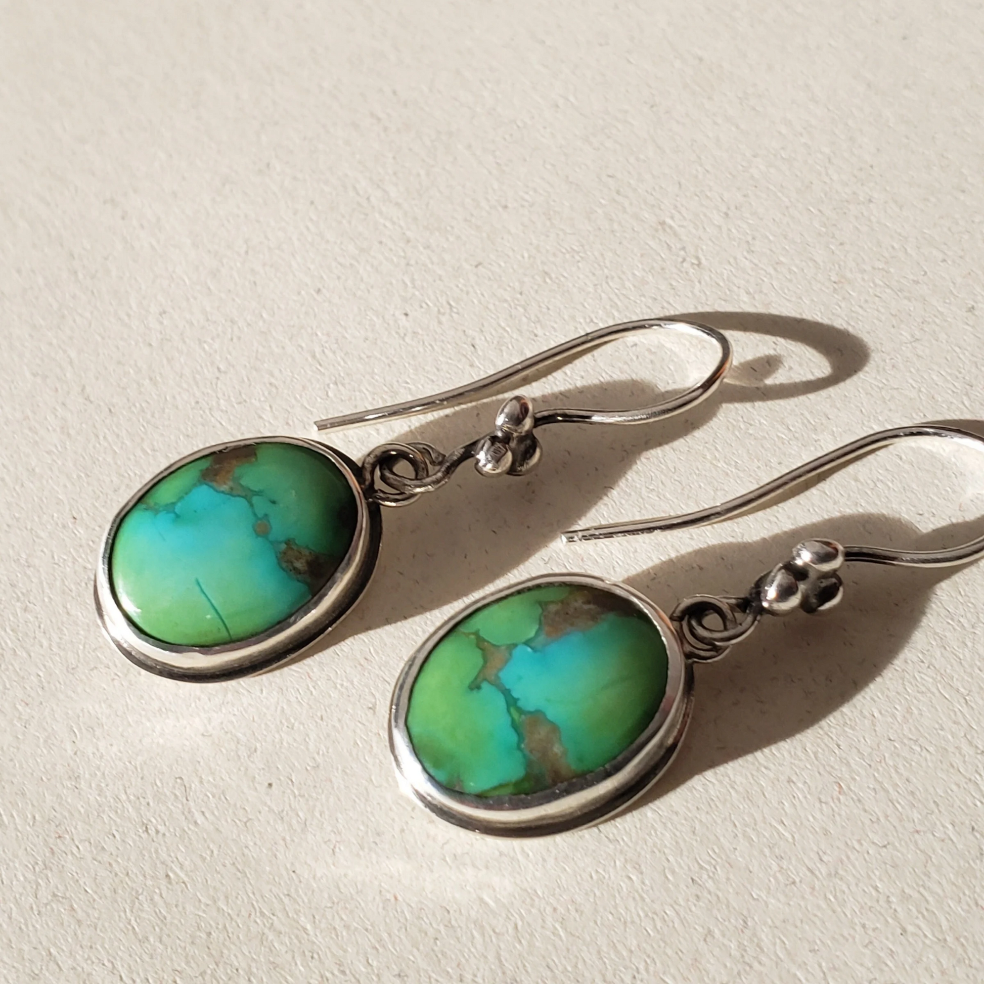 Green blue turquoise earrings against beige background 