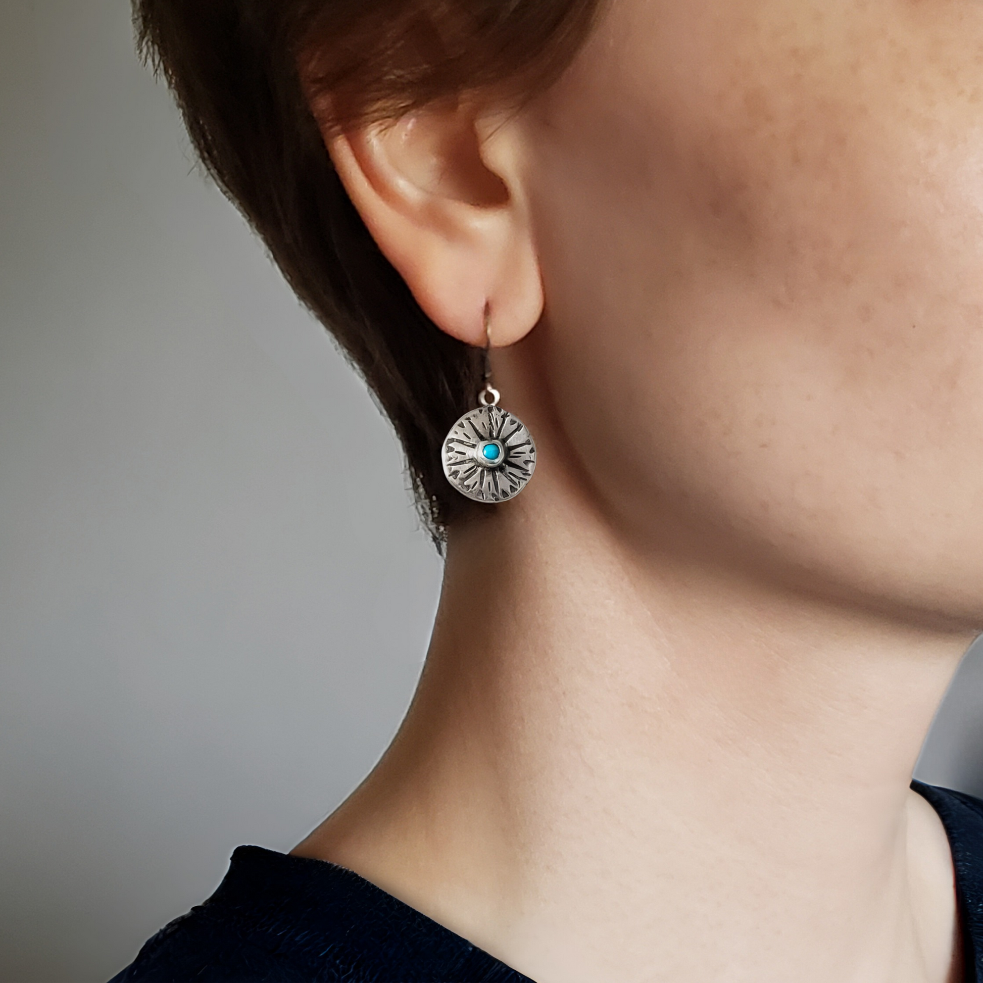 Right facing woman wearing small handmade sterling disc earrings with turquoise gemstone center hung on silver lever backs
