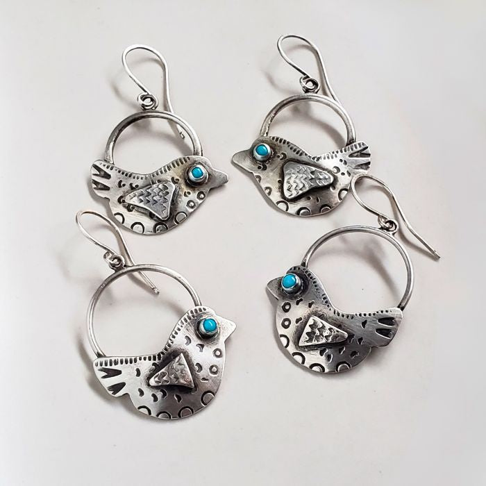 Set of silver bird-shaped earrings with turquoise stones on a light gray background